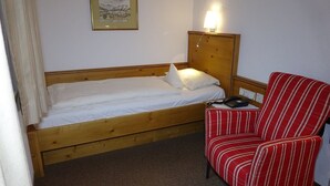 A single wooden bed with white linens, a bedside table with a lamp, and a striped armchair. - Interest of Bavaria (Oberstaufen)