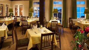 A dining area with tables set for two, wooden chairs, and green curtains. - Interest of Bavaria (Oberstaufen)