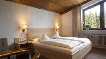 Ein Hotelzimmer mit einem hölzernen Bett, zwei Nachttischlampen, einem Nachttisch, einem Fenster mit Vorhängen und einer Heizung.