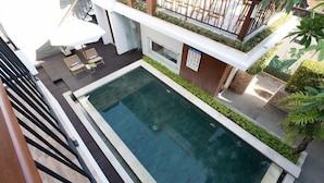 A modern outdoor swimming pool with a wooden deck, lounge chairs, and a small table. - Mahesa Home Seminyak (Seminyak)