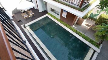 A modern outdoor swimming pool with a wooden deck, lounge chairs, and a small table.