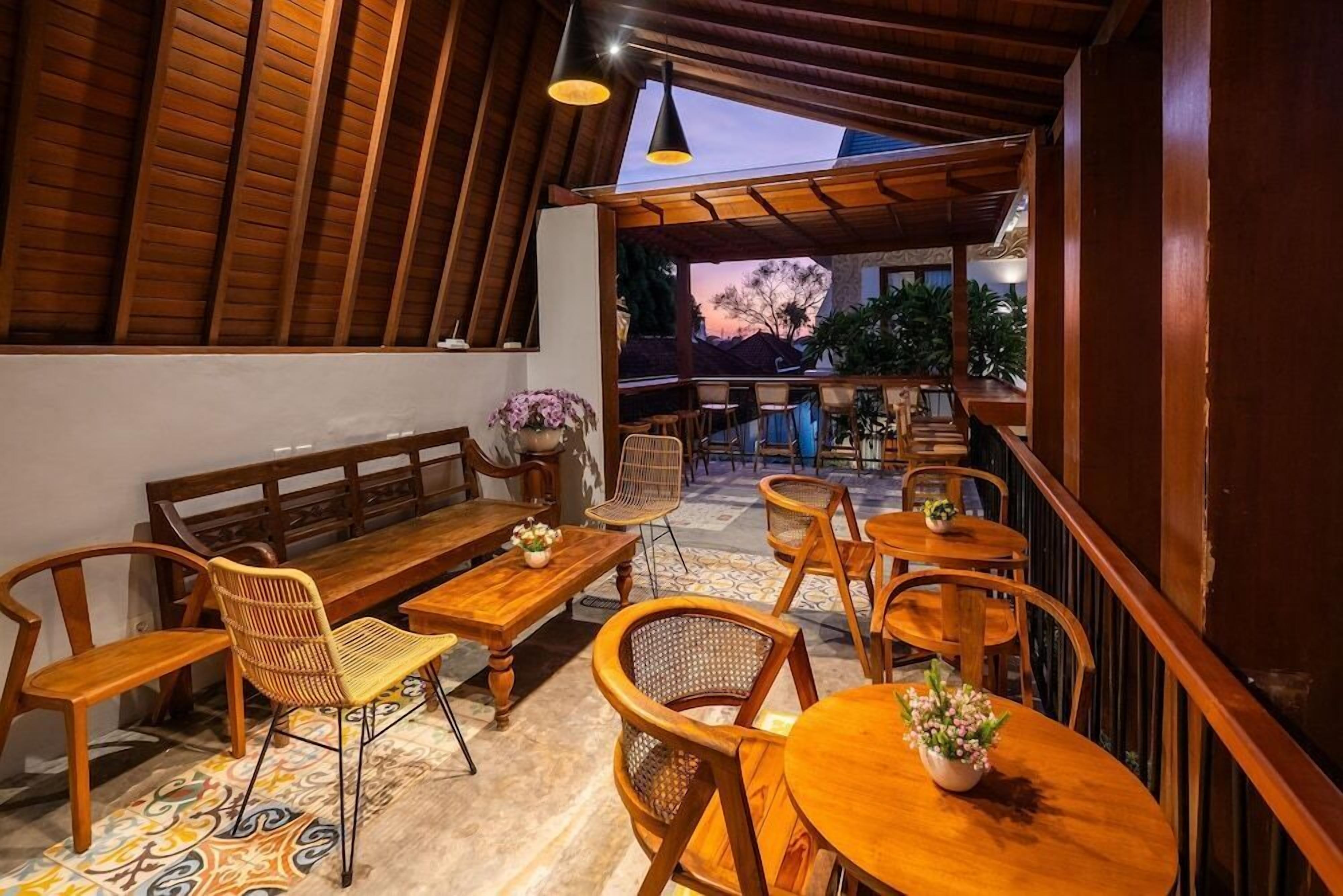 An outdoor seating area with wooden furniture, including benches and tables, arranged under a wooden pergola.