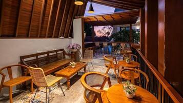 An outdoor seating area with wooden furniture, including benches and tables, arranged under a wooden pergola.