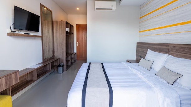 A modern hotel room with a large bed, a flat-screen TV mounted on the wall, a wooden wardrobe, and a built-in bench. - Mahesa Home Seminyak (Seminyak)