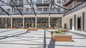 Une cour spacieuse dotée d’une architecture moderne, de grandes fenêtres et de jardinières en bois ornées de plantes vertes.