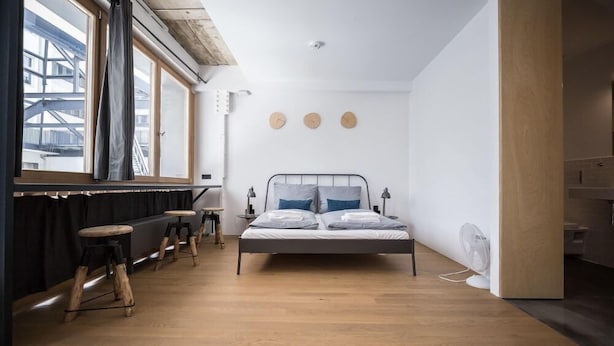 Une chambre à coucher moderne avec un lit, des tabourets en bois, une fenêtre et un radiateur.