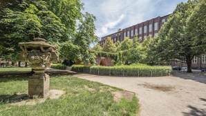 Une cour avec une fontaine en pierre, une végétation luxuriante et un bâtiment en briques en arrière-plan.