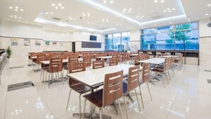 Una cafetería amplia con varias mesas y sillas, ventanas grandes y un diseño moderno en el techo.