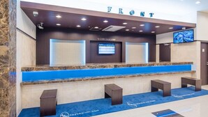 Un mostrador de recepción con una pantalla digital, un televisor de pantalla plana y un cartel que dice "FRONT".