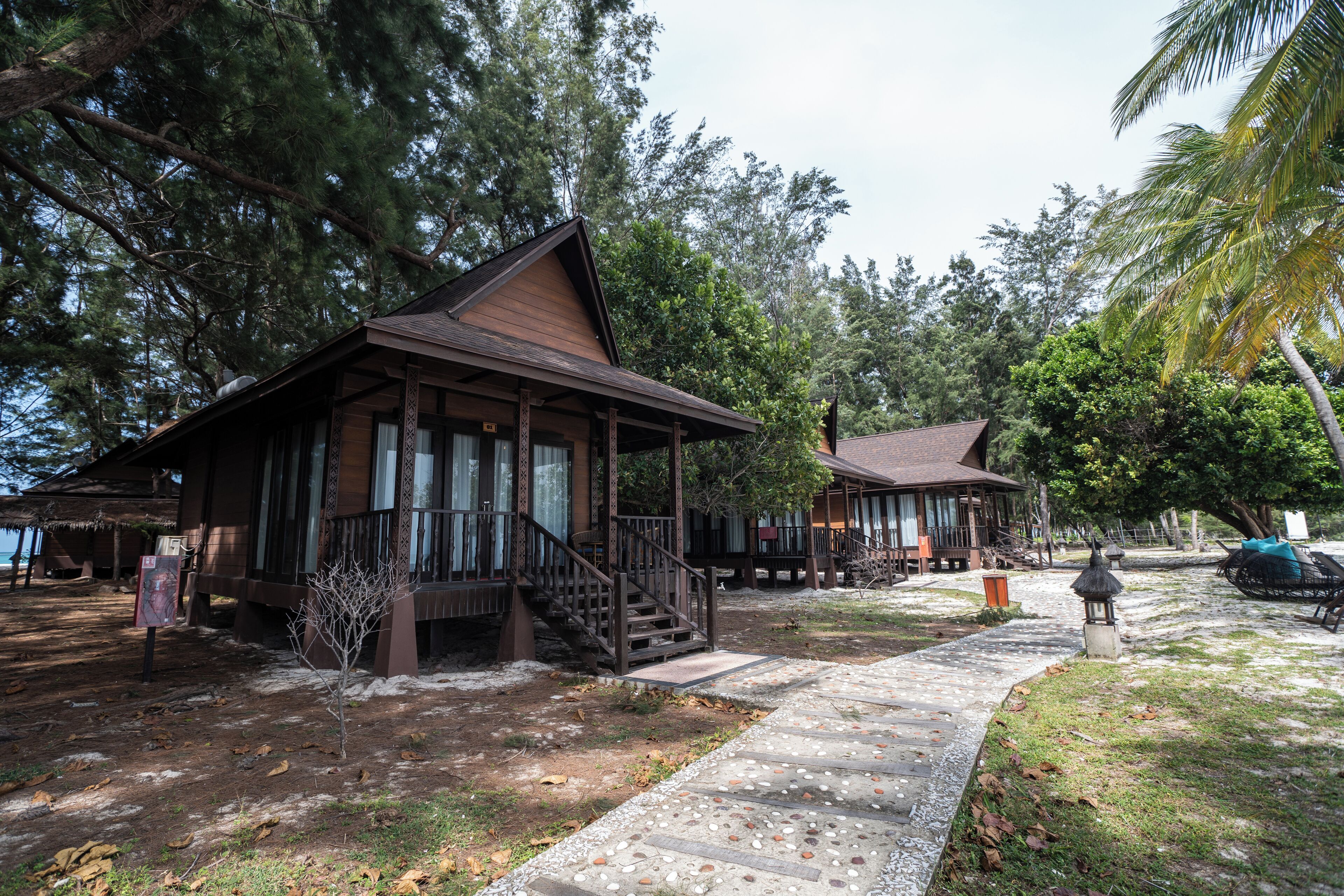 A wooden lodge with a porch and staircase, surrounded by trees and a pathway.