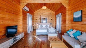 En mysig interiör i en stuga byggd av timmer, med ett trägolv, en säng med en sänggavel, en soffa, en tv på ett stativ och en takfläkt.