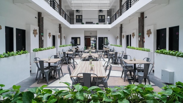 A spacious indoor dining area with multiple tables and chairs, white walls, and a central open space. - Sans Hotel Fiffa Premiere Malang (Malang)
