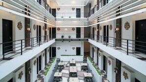 A multi-level atrium with a central open space, surrounded by dining tables and chairs, and balconies on each level. - Sans Hotel Fiffa Premiere Malang (Malang)