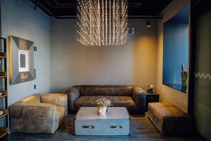 A modern living room with a leather sofa, a coffee table with a vase, and a unique chandelier. - Hotel Alice and Trunk (Jeju City)