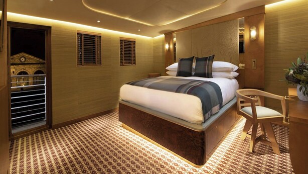 A modern hotel room with a large bed, a small desk, and a view of a building through a window. - Fingal A Luxury Floating Hotel (Edinburgh)