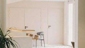 Un salón moderno y minimalista con un ventanal grande, un comedor con una cocina al fondo y una alfombra estampada en el suelo.