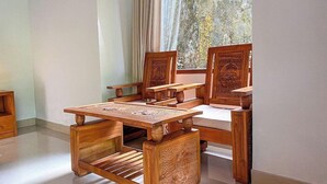A traditional wooden dining set with intricate carvings, positioned in a room with a large window and curtains. - Bali Jungle Huts (Sebatu)
