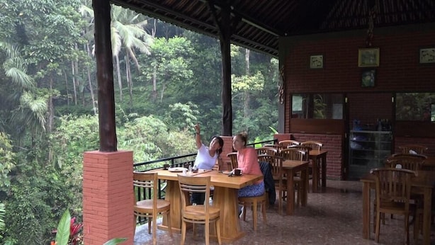 An outdoor dining area with wooden tables and chairs, surrounded by lush greenery and a brick wall. - Bali Jungle Huts (Sebatu)