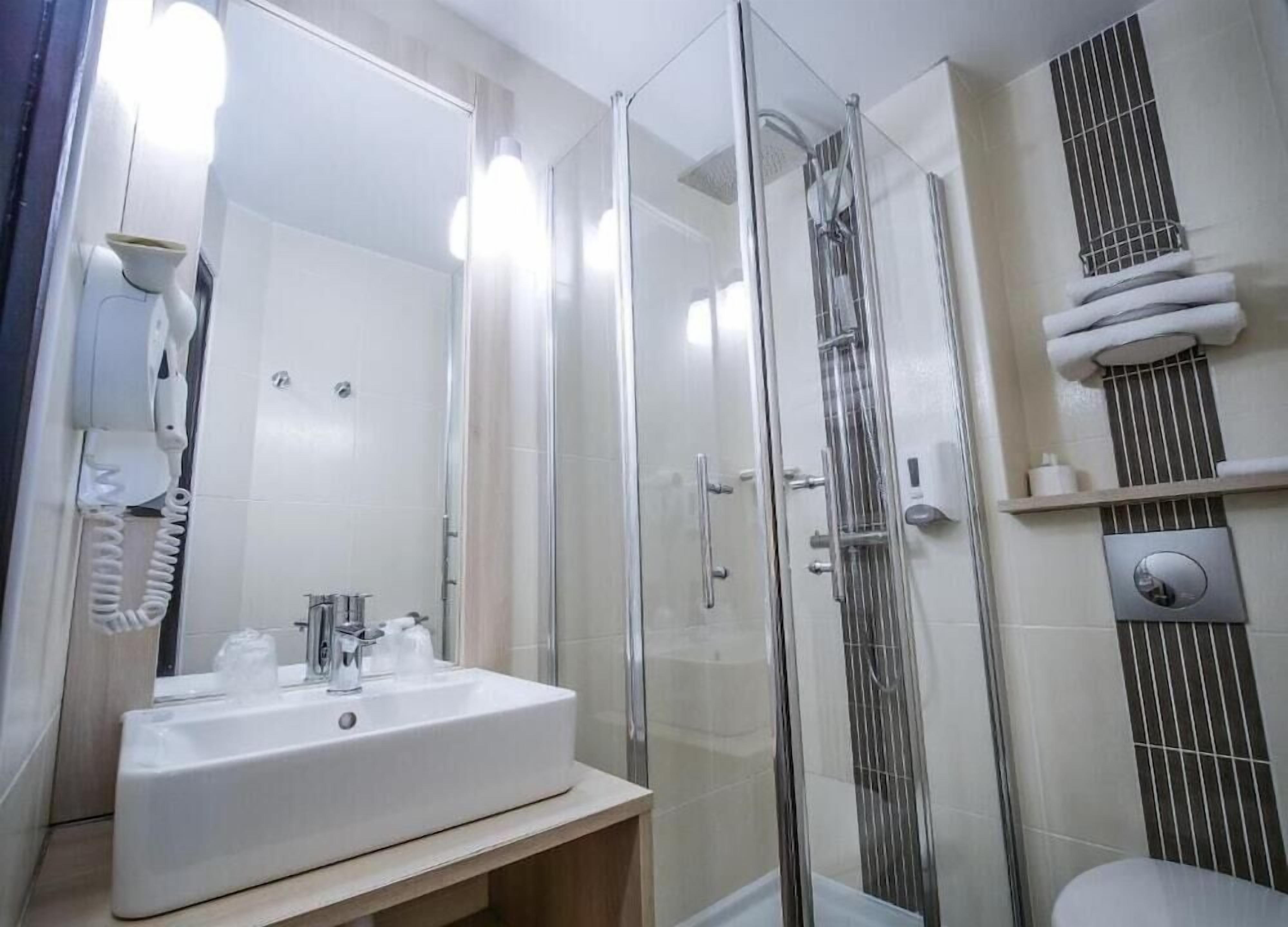 A modern bathroom with a glass-enclosed shower, a white sink with a mirror, and a towel rack.