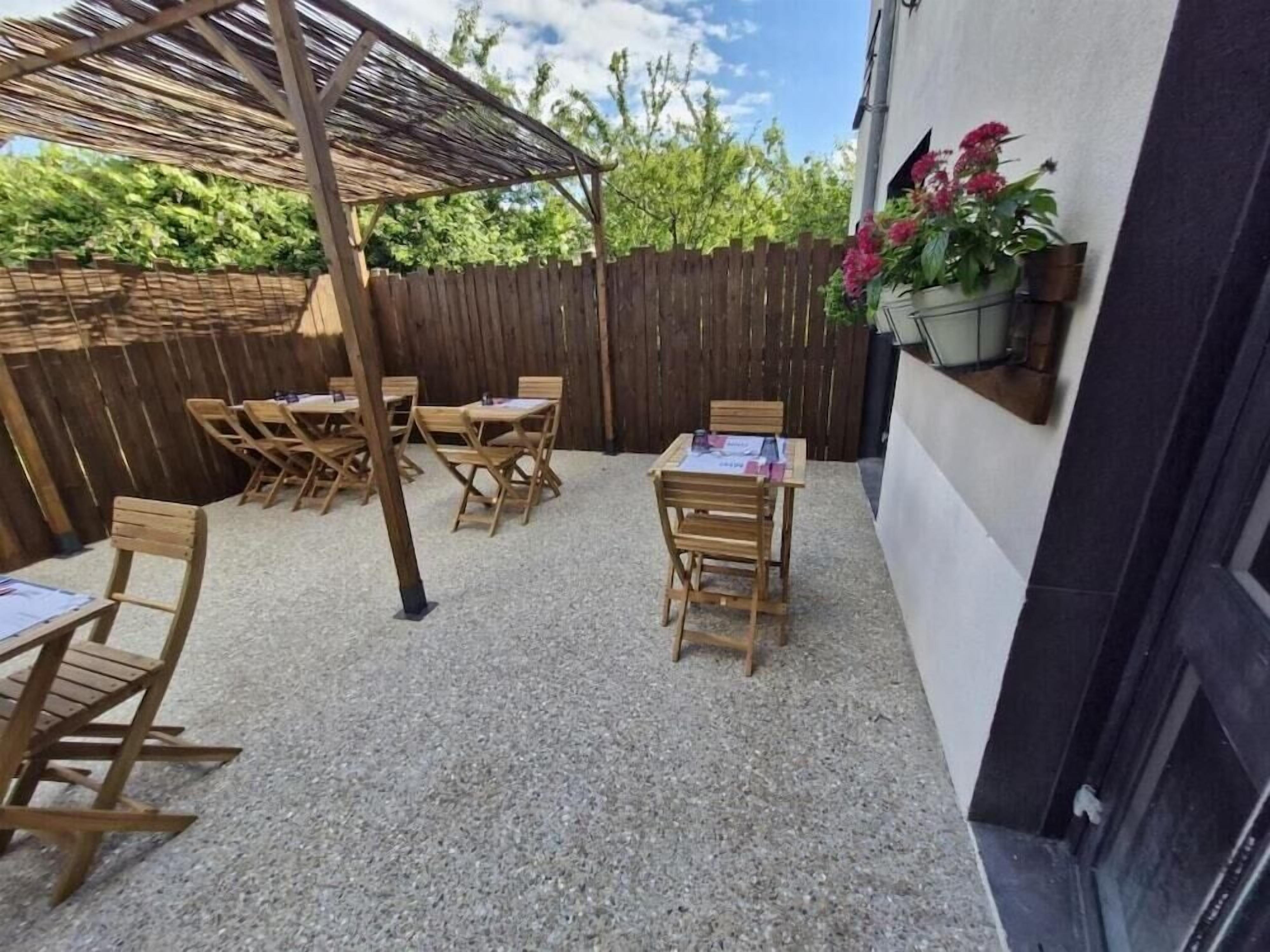 Un patio al aire libre con mesas y sillas de madera, una pérgola y una valla de madera.