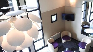 Ein moderner Lounge-Bereich mit einem einzigartigen, kugelförmigen Kronleuchter, bequemen Sitzgelegenheiten mit violetten Kissen und einem wandmontierten Flachbildfernseher.