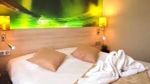 Ein Hotelzimmer mit einem Bett, zwei Kissen, einer Wandleuchte und einer Wand mit einer reflektierenden Oberfläche in Grün und Gelb.