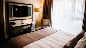 Une chambre d’hôtel avec un grand lit, un bureau doté d’un téléviseur à écran plat, une chaise et une lampe.
