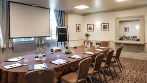 A conference room with a long table, chairs, a projector screen, and framed pictures on the walls. - Brandshatch Place Hotel and Spa (Longfield)