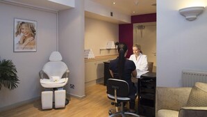A modern spa room with a massage chair, a reception desk, and a waiting area with a sofa. - Brandshatch Place Hotel and Spa (Longfield)