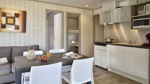 Un espace de vie compact comprenant un coin repas, une kitchenette et une chambre visible avec un lit superposé.