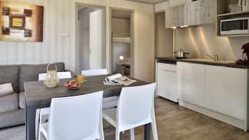 Un espace de vie compact comprenant un coin repas, une kitchenette et une chambre visible avec un lit superposé.
