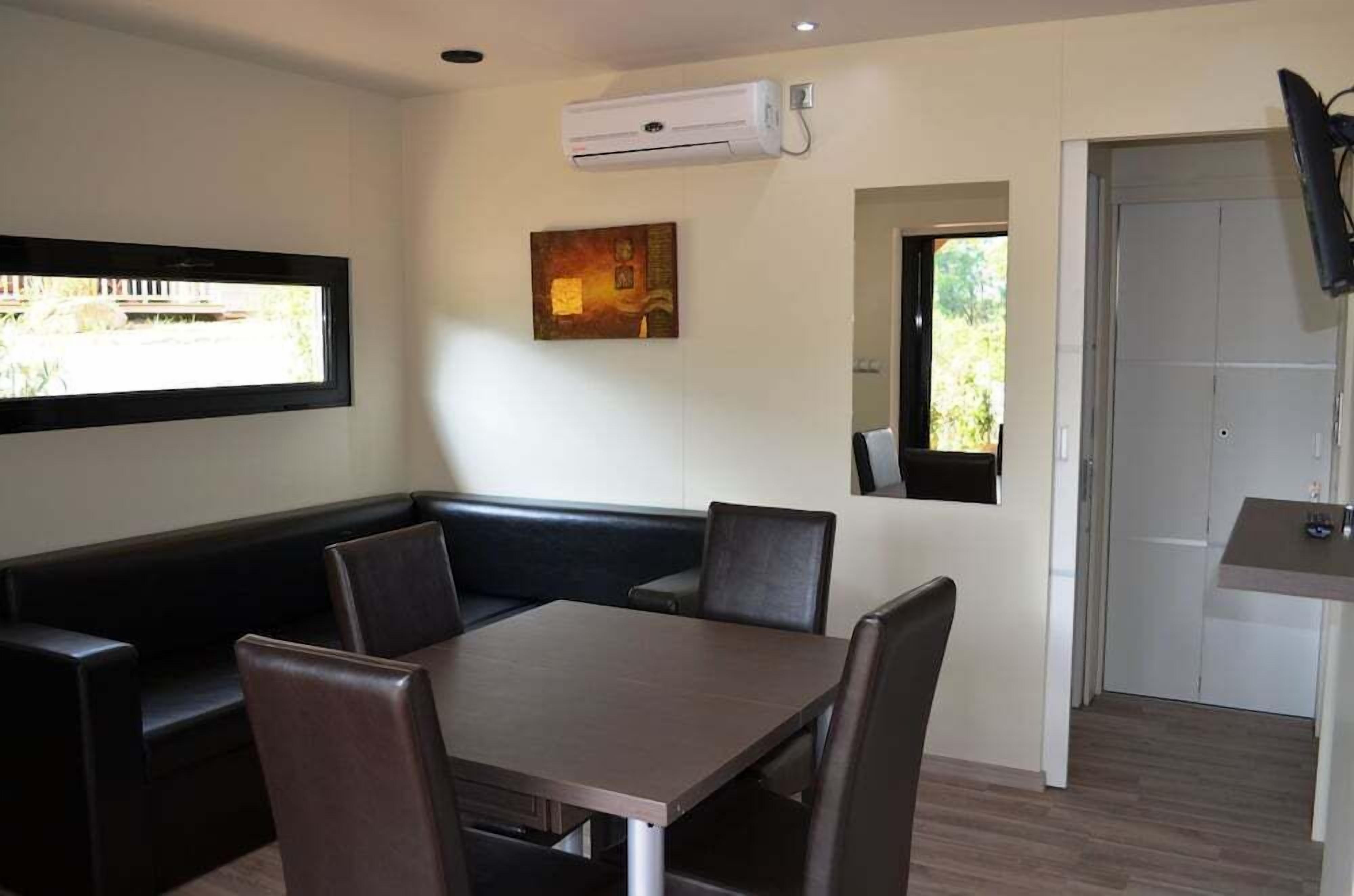 Un comedor con una mesa y sillas, un banco acolchado negro, un cuadro en la pared y un equipo de aire acondicionado.