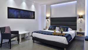 Une chambre d’hôtel moderne avec un grand lit, des lampes de chevet, une table de chevet, une chaise et une œuvre d’art encadrée au mur.