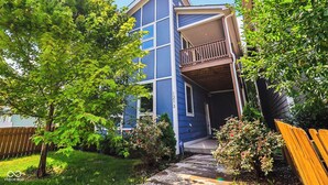 A two-story blue building with a balcony, surrounded by trees and a wooden fence. - Modern Oasis in Heart of Fountain Square, 4BR/3BA (Indianapolis)