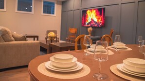A dining area with a round table set for four, a television mounted on the wall, and a sofa in the background. - Modern Oasis in Heart of Fountain Square, 4BR/3BA (Indianapolis)