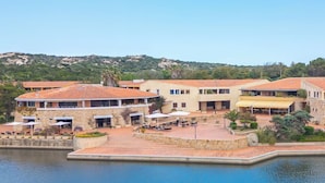 A coastal hotel with a pool, outdoor seating, and a view of the sea. - Residence Costa Serena (Palau)