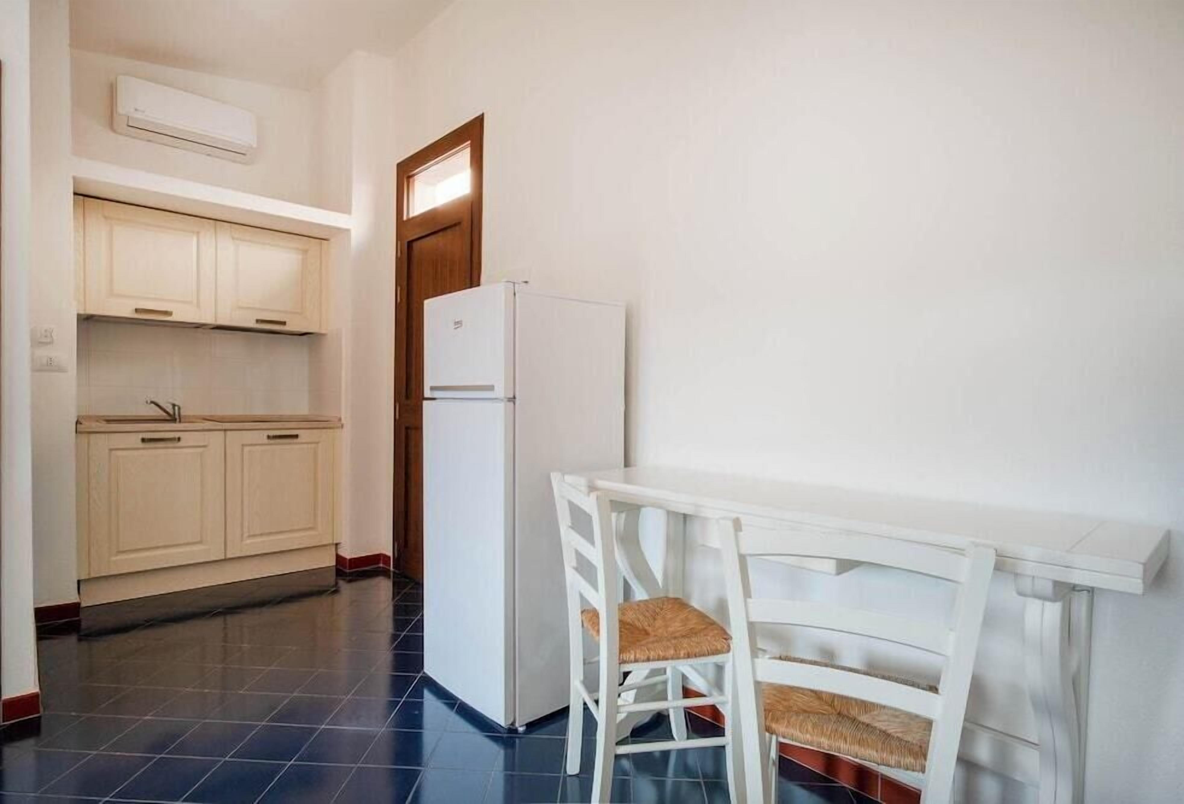 A small kitchen with a refrigerator, a sink, and a dining table with chairs.