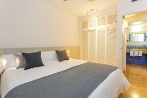 A bedroom with a bed, pillows, a bedside table, a wardrobe, and a bathroom visible through an open door. - Apartamentos Ses Eufabietes (Formentera)