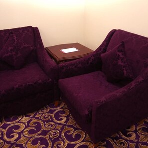 Une pièce avec deux fauteuils violets, une petite table d’appoint en bois sur laquelle se trouve un papier, et un tapis à motifs.