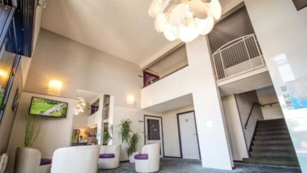 A modern lobby with a staircase, seating areas, and a television screen. - Hotel Inn Design Langres Resto Novo (Langres)