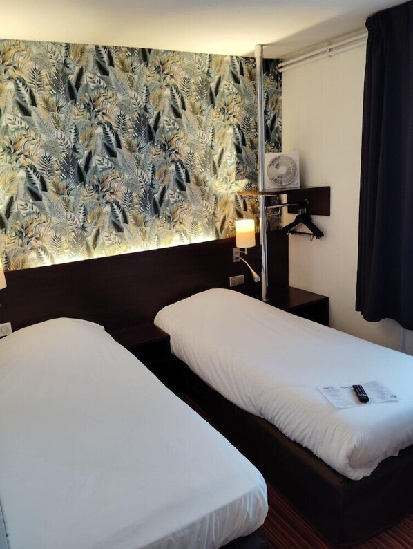 Une chambre d’hôtel avec deux lits simples, un climatiseur fixé au mur, une lampe de chevet et un rideau foncé.