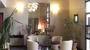 A modern lobby with a large mirror, a round coffee table, and three white armchairs with purple cushions. - Hotel Inn Design Langres Resto Novo (Langres)