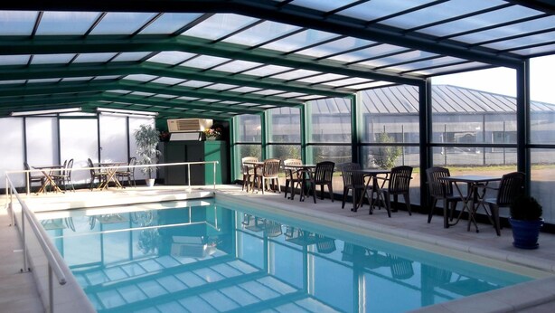 A covered swimming pool with seating areas and a view of a greenhouse in the background. - Jum Hotel - Auberge Des 3 Jumeaux (Saints-Geosmes)