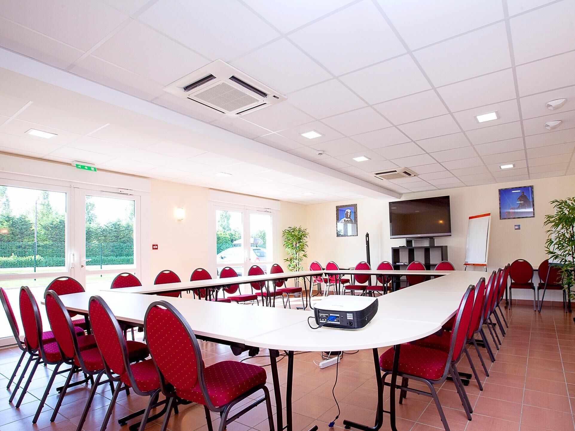 Een vergaderzaal met een lange tafel, rode stoelen, een projecter en een groot scherm.