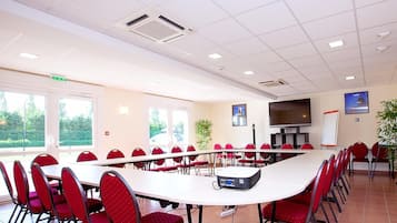 Ein Konferenzraum mit langem Tisch, roten Stühlen, einem Projektor und einer großen Leinwand.