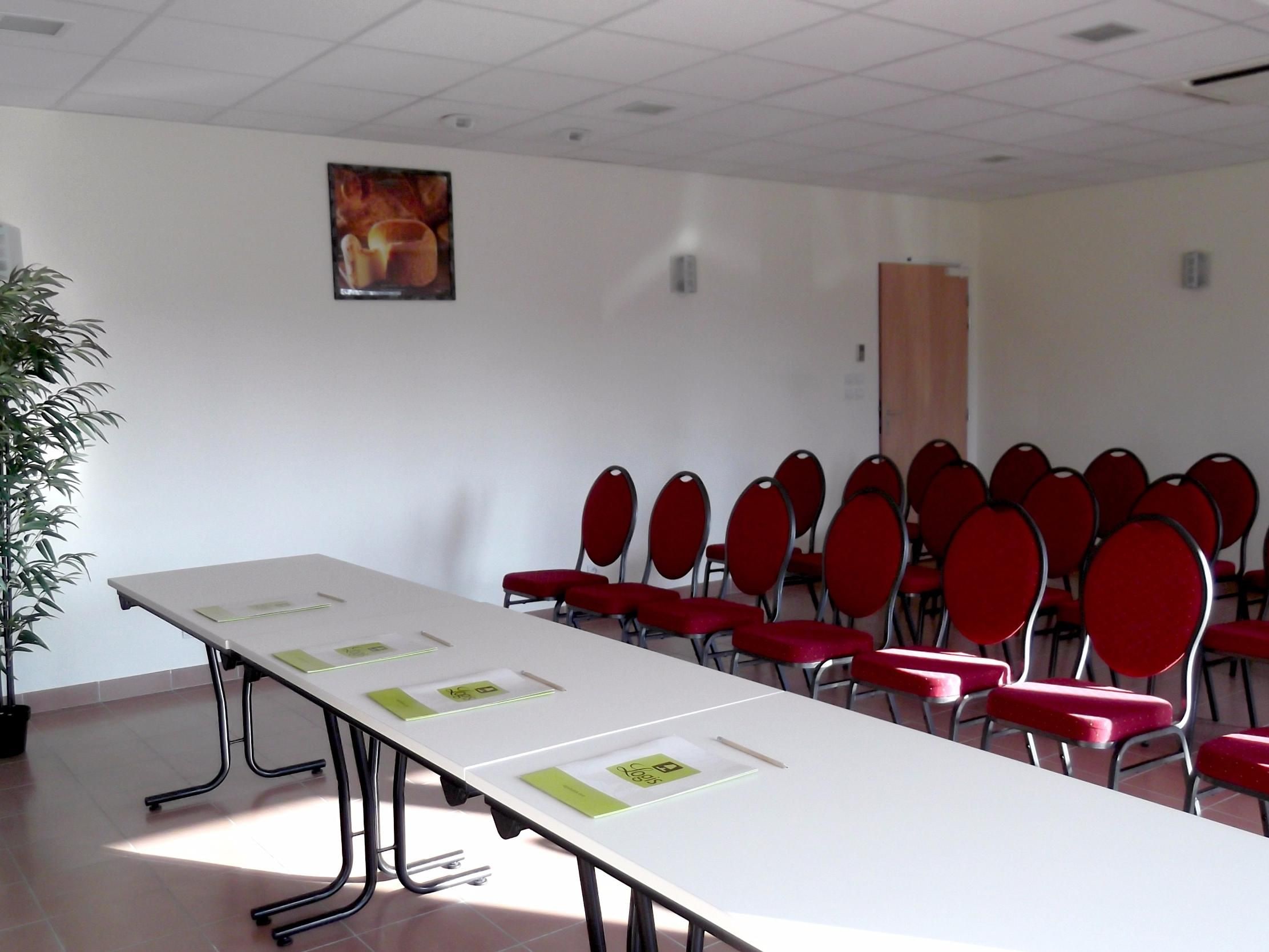 Ein Konferenzraum mit langem Tisch, roten Stühlen und einem Blumentopf.