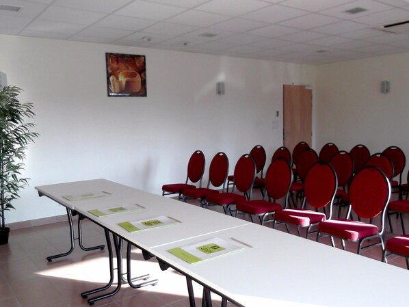 Un salón de conferencias con una larga mesa, sillas rojas y una planta en maceta.