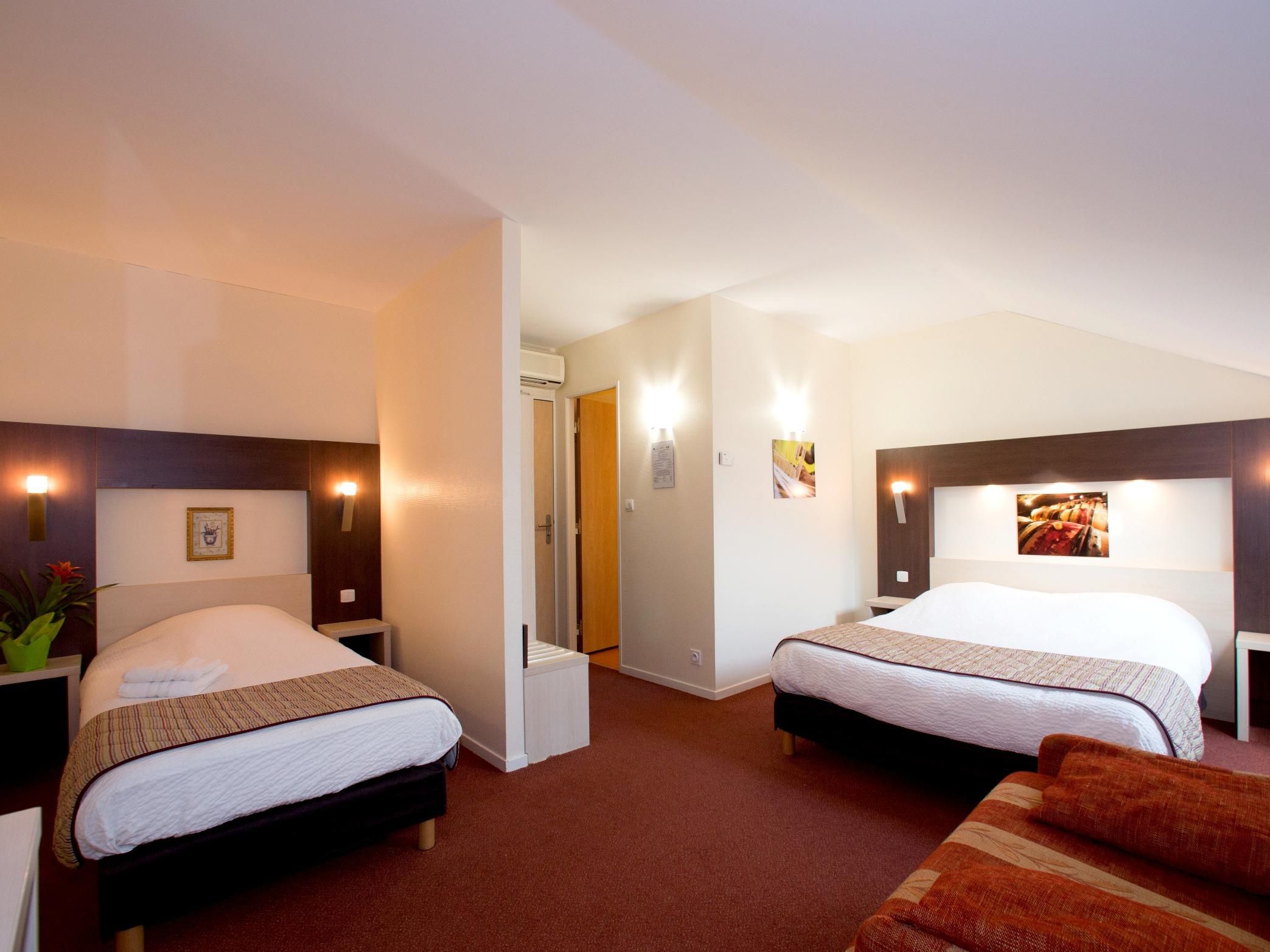 Une chambre d’hôtel avec deux lits, un petit coin salon et une porte donnant sur la salle de bain.
