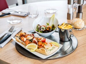 Una mesa de comedor con un plato de mariscos, una ensalada, papas fritas y un croissant.