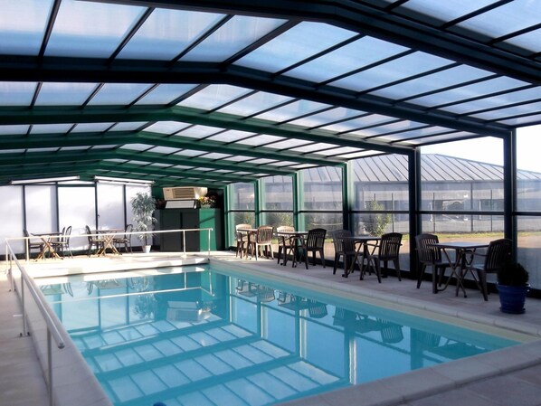 A covered swimming pool with seating areas and a view of a greenhouse in the background. - Jum Hotel - Auberge Des 3 Jumeaux (Saints-Geosmes)